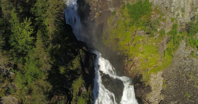 Aerial: Drone moving over rainbow appearing on waterfall flowing through rocky cliff - Borgund, Norway