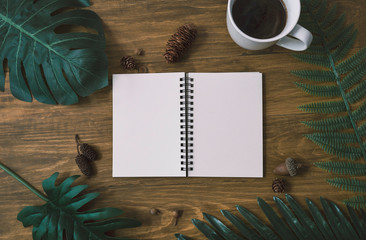 Background top view of notebook, cup of coffee, green leaves pine cones on wood table background....