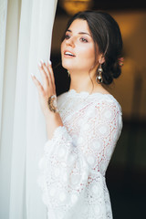 Fototapeta premium Beautiful bride brunette young woman in white lace dress near the window, close up portrait