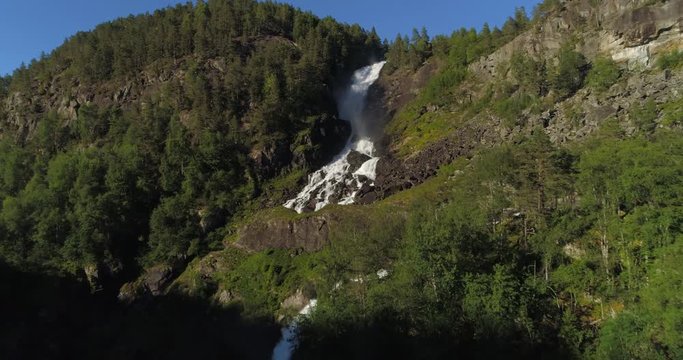 Aerial: Drone approaching over waterfall streaming from mountain in forest - Borgund, Norway