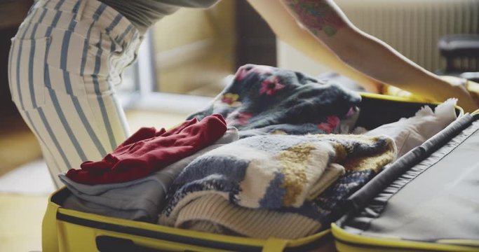Coseup of woman packing a luggage on bed