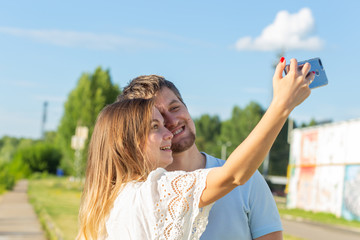 Beautiful romantic couple on nature background. Attractive young woman and handsome man are making selfie, smiling and looking at camera.