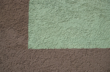 Brown and green fragment of the wall of the building in the form of a right angle on the left with applied decorative plaster "bark beetle"