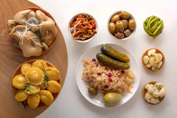 Salted mushrooms and squash in wooden plates on a background of fermented products on a white table. Close-up. Top view