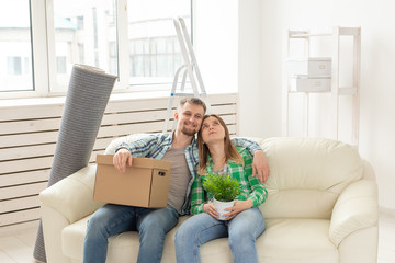 Positive young couple in love husband and wife are sitting on the couch in the new living room during the move and enjoy their new home. Mortgage concept and moving to a new home.