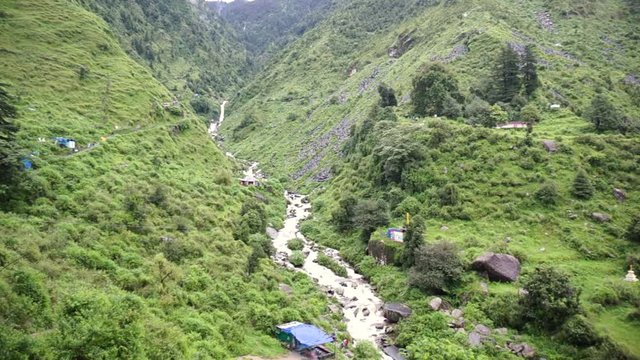 Panning shot showing the lush plant covered mountains and river streams of the himalayas in McLeodganj hill station near Bhagsu Falls