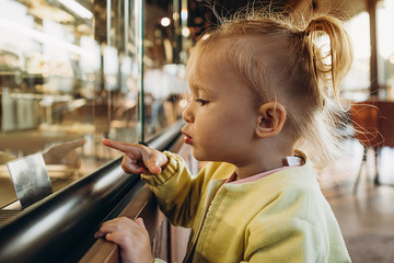 a little girl points her finger at the pastry shop, choosing the dessert she likes