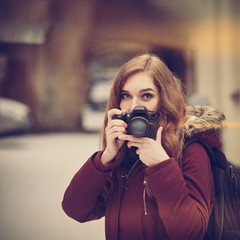 Young attractive woman photographer taking photos in winter city, image with warm vintage toning