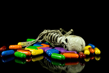 Human like rubber skeleton laying on colored pills , conceptual image about illness , death and pharmaceutical industry