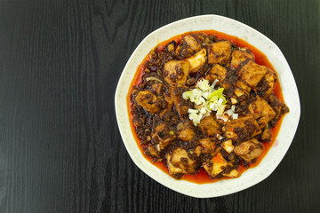 Homemade Mapo Tofu with minced green onions, Hot and spicy chinese food on white plate and black wood table with copy space in the leftside.