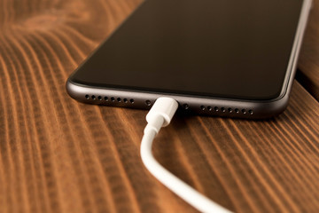 Smartphone on charge . On the  wooden table . Close up.