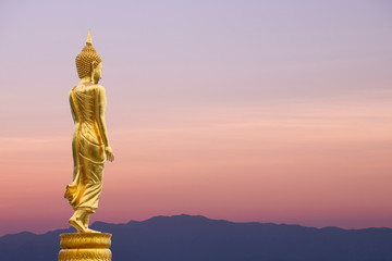 Buddha statue standing on sunset sky background.