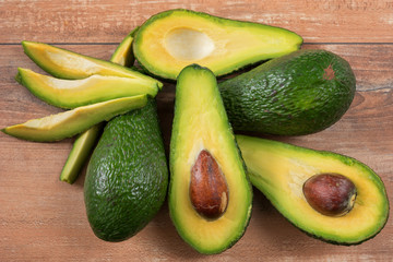 Close-up photo of fresh sliced avocados, brown seeds visible on brown wooden background. Vegetarian food concept, vintage style, avocado background.