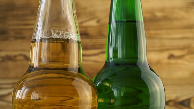 Two beer bottles rotating on wood texture surface. Close up of alcohol drink in transparent and green bottle.