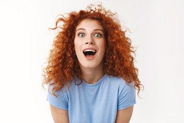 Charismatic beautiful redhead woman with curly hairstyle, making surprising and amused expression,...