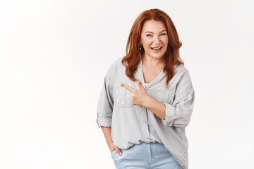 Confident middle-aged redhead european woman telling about interesting product recommend check-out promo smiling toothy self-assured pointing left index finger assuring you like it, white background