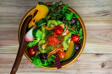 Top view various fresh healthy mixed vegetables salad with flying fish roe on top in wooden bowl and wood salad spoon on wooden background.