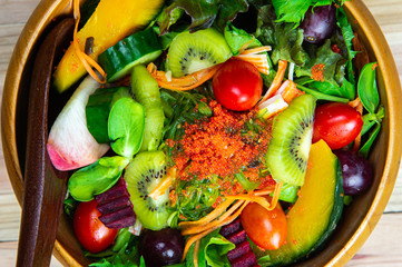 Top view various fresh healthy mixed vegetables salad with flying fish roe on top in wooden bowl and wood salad spoon on wooden background.