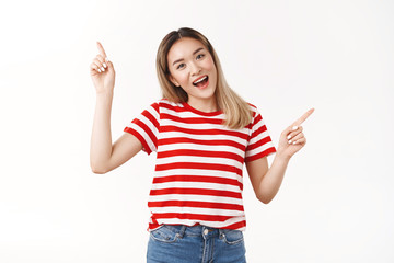 Cheerful excited asian blond girl likes shopping summer trip goods pointing up right sideways tilting head joyful thrilled smiling broadly good mood amazing variaty choices, standing white background