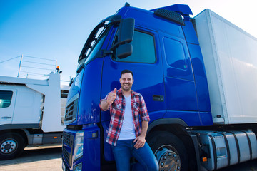 Professional truck driver in front of long transportation vehicle holding thumbs up ready for a new...