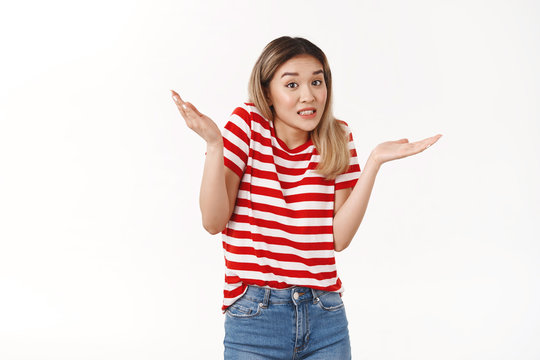 Yikes sorry my fault. Awkward silly timid blond asian girl new team member apologizing making mistake oops raise hands sideways clenching teeth stooping worried, standing confused white background