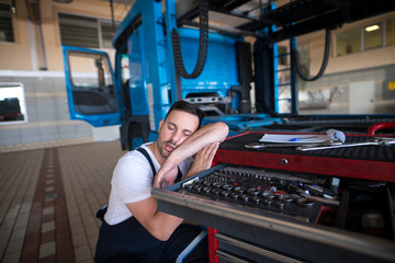 People sleeping at their job. Exhausted vehicle mechanic falling asleep in his workshop. Overworked and tired people.