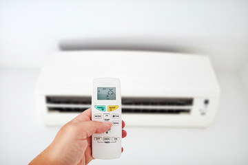 Modern airconditioner unit with a hand holding a remote.