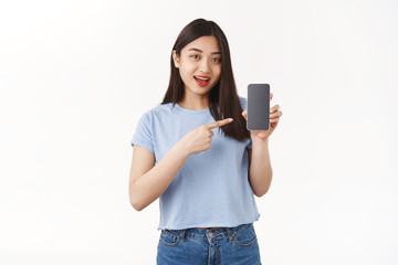Optimistic good-looking asian girl dark hair introduce app hold smartphone pointing cellphone screen speaking about interesting application game stand white background show social media profile