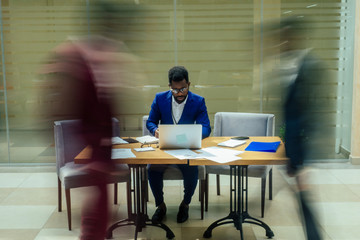 africa american business man working with laptop,blurred people walking next to him in big office