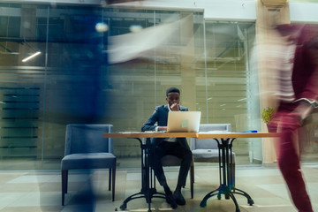 africa american business man working with laptop,blurred people walking next to him in big office...