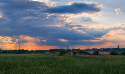 Natural sunset over field or meadow. Bright dramatic sky and dark ground.