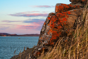 Evening seascape. The coast of the Anadyr estuary. Rocks are covered with lichen. A boat is floating in the distance. Cape Alexander, Chukotka, Siberia, Far East Russia. Arctic landscapes and nature.