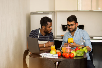 Two men using laptop in kitchen