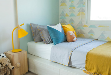 Kid bedroom in blue and yellow tone pillow with many doll on bed. 