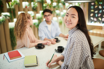 Multi-ethnic group of students studying together in cafe, focus on smiling Asian girl looking at camera, copy space