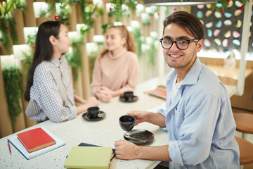Multi-ethnic group of students studying together in cafe, focus on mixed-race young man smiling at camera, copy space