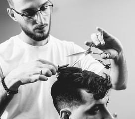 Young man with trendy haircut at barber shop. Barber does the hairstyle and beard trim.