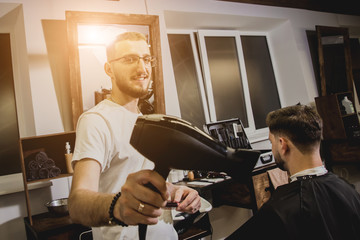 Young man with trendy haircut at barber shop. Barber does the hairstyle and beard trim.
