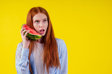 crazy redhaired ginger woman with watermelon imagine that she talking by phone in yellow background studio wall