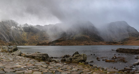 Beautiful moody Winter landscape image of Llyn Idwal and snowcapped Glyders Mountain Range in Snowdonia