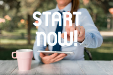 Text sign showing Start Now. Business photo text do not hesitate get working or doing stuff right away Female business person sitting by table and holding mobile phone