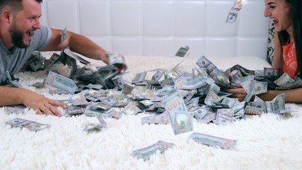 Female and male throw at each other a lot of banknotes of dollars on the bed, slow motion, top view