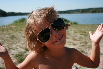 little girl sitting on the lake in sunglasses and smiling