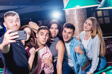 A group of friends makes a selfie at the pool table. Posing with a cue in their hands.