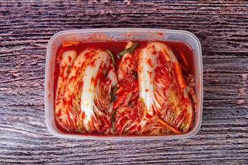 The fermented kimchi is packed in a plastic food container placed on a wooden floor.
