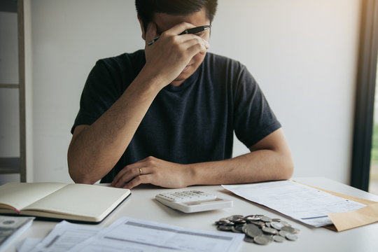 Asian men are stressed about financial problems, with invoices and calculators placed on the table while having stress on problems with home expenses.