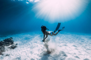 Freediver girl with fins dive over sandy sea.