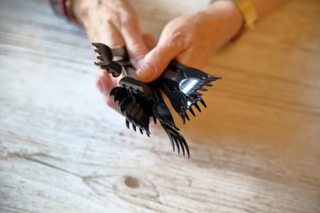 Black plastic disposable forks in senior lady hands on wooden table, close up, concept of non-ecological life style