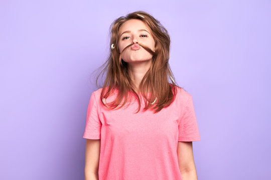 Portrait Shot Of Cheerful Funny Girl Having Playful Mood, Making Moustache With Her Hair, Joking And Having Great Time With Friends At Pyjamas Party, Lots Of Feathers In Messy Hair After Pillow Fight.