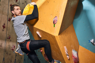 Fototapeta na wymiar Athletic young boulderer without forearm rock climbing in bouldering sport center, sweaty and tired, never gives up, going to finish difficult ascend, strong-willed and positive person.
